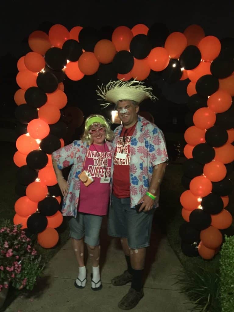 Two party guests posing beneath an orange and black balloon arch
