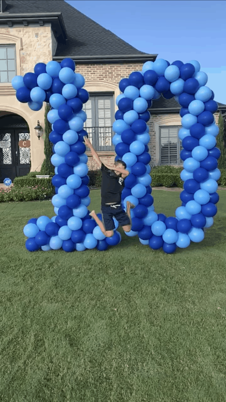 a man jumping in the air in front of a large number made of balloons
