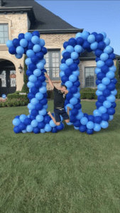 a man jumping in the air in front of a large number made of balloons